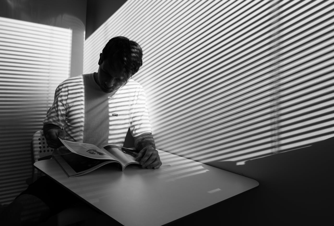 Dramatic black and white image of a man reading indoors with striped shadow pattern.