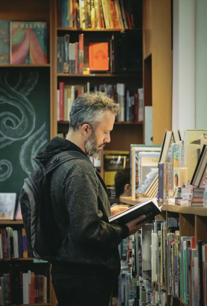 Adult man reading a book in a cozy bookstore, enjoying a quiet moment surrounded by books.